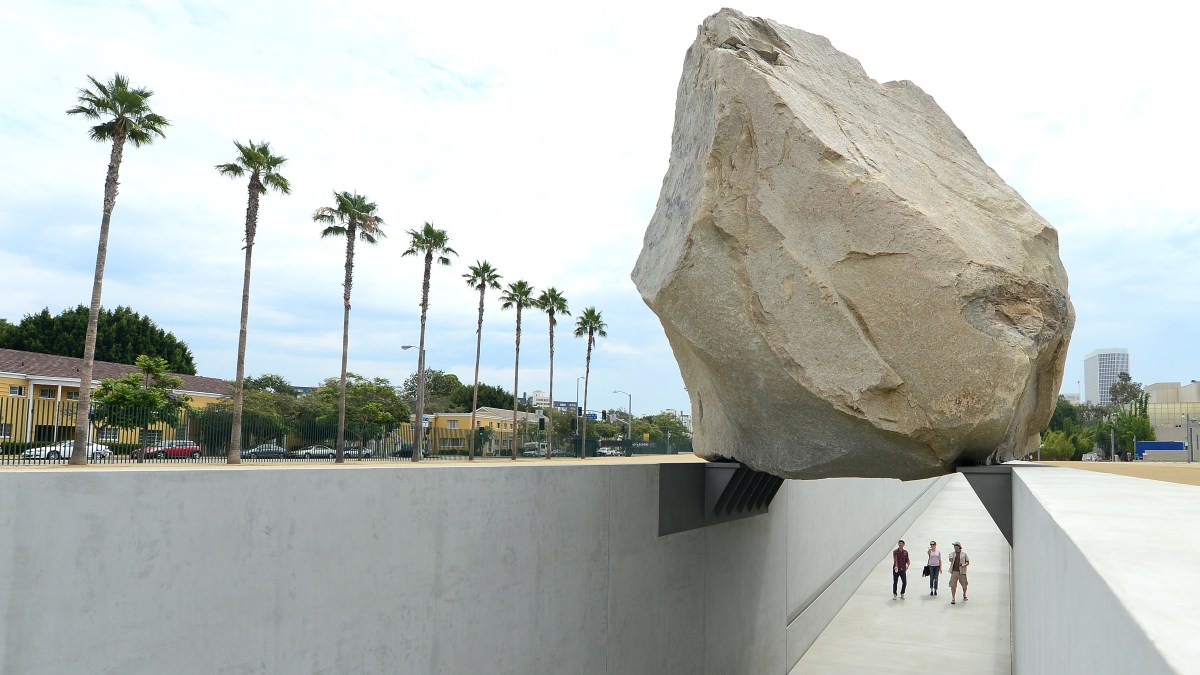 People walk a path beneath a giant rock