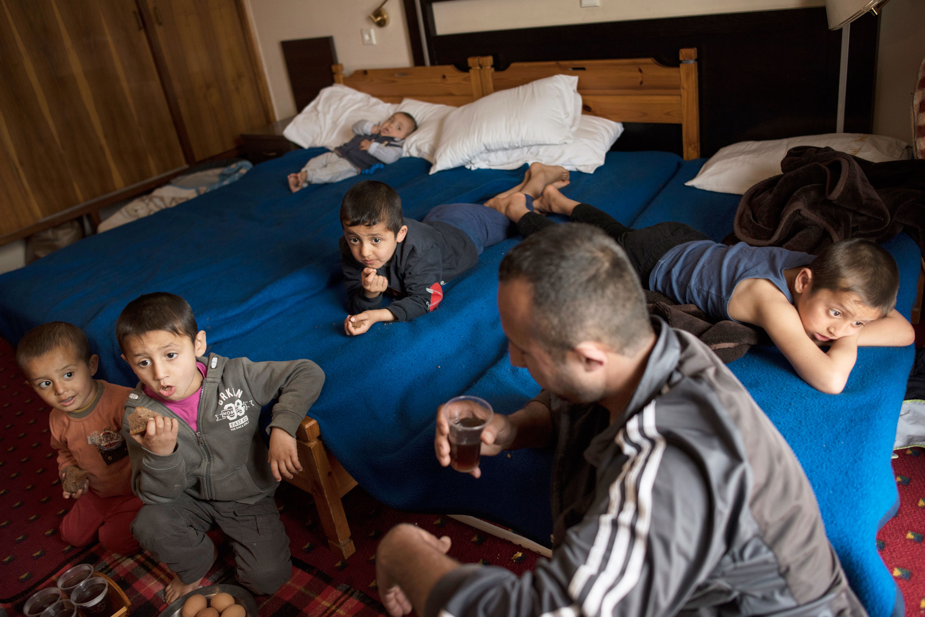 Minhel and the boys watch TV in a hotel room in Kastoria, Greece. Their lives are still in limbo