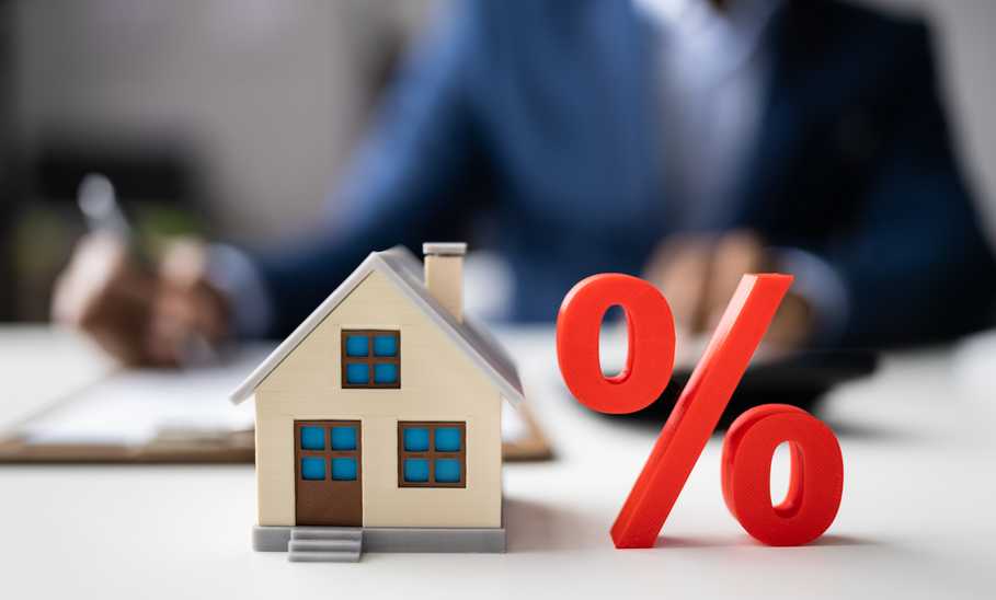 percentage sign next to a model home, in the background man signing on a mortgage