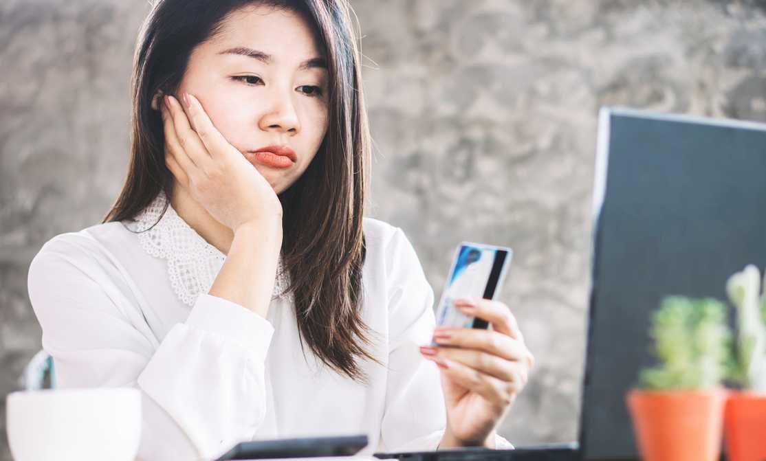 asian woman looking at credit card and bill looking sad