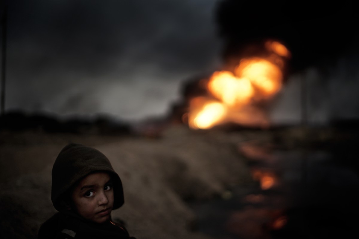 A small boy watches one of the estimated 19 oil wells which has been set at fire by IS in the city Qayyara, south of Mosul. The dense plumes of smoke are emanating from multiple sites about 30 miles (50 km) south of Mosul. The fires were deliberately set by ISIS militants before abandoning the city. The smoke has been persistent over the past three months, blotting out the sun hours before nightfall and creating major health issue for mainly the children in the area.