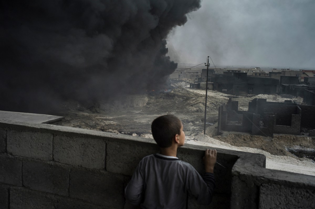 A boy looks out from the rooftop of his house as an oil well burns right next to it in Qayyarah, a town about 60 km south of Mosul. The town fell to ISIS in June 2014 and was recaptured by the Iraqi forces in August 2016, while leaving Qayyarah ISIS burned the oil wells in and around the city.